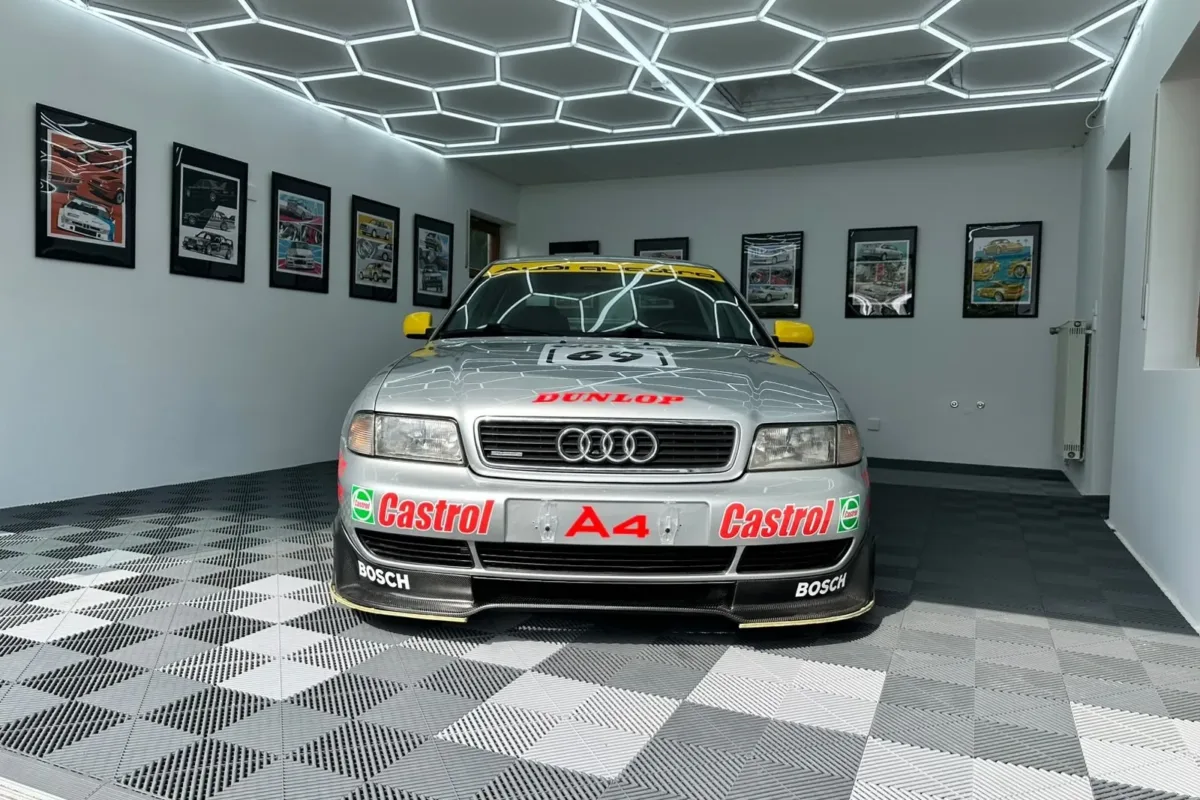 Audi A4 B5 STW frontal: Castrol- und A4-Schriftzug auf der Frontschürze, Bosch-Frontspoiler und gelbe Außenspiegel, in der Halle mit Wabenbeleuchtung