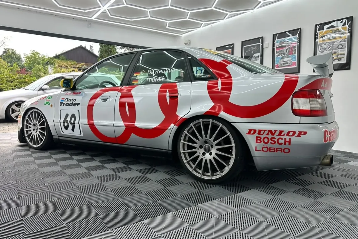 Audi A4 B5 STW mit Heckflügel, großen roten Audi-Ringen und Startnummer 69, schräg von hinten in der Halle mit geöffnetem Tor