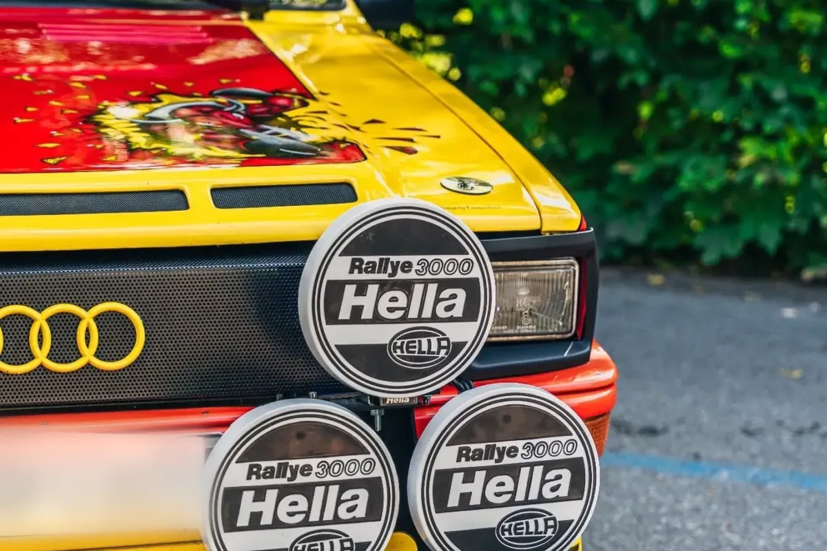 Detail der Front des Audi quattro: Hella-Rallye-3000-Zusatzscheinwerfer, gelbe Frontschürze mit Lüftungsschlitzen und bemalte rote Motorhaube