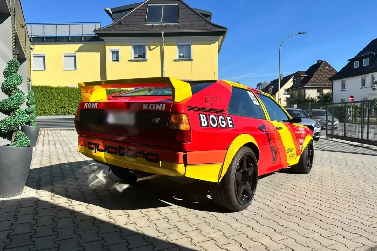 Heck des Audi quattro im Rallye-Design mit BOGE- und quattro-Schriftzug und großem Heckflügel vor dem Werkstattgebäude