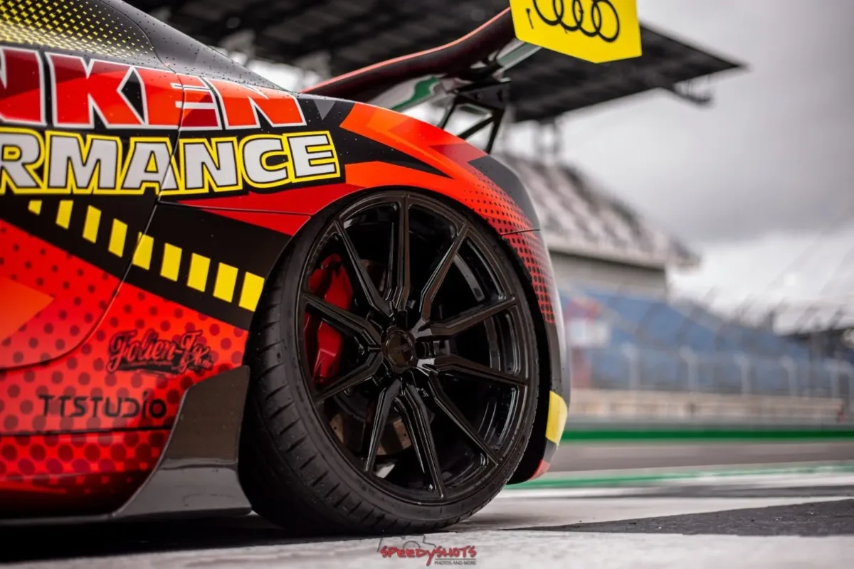 Detailaufnahme des Audi R8 V10 Plus: Hinterrad mit schwarzer Felge und rotem Bremssattel, Folierung im Franken-Performance-Design und Heckflügel vor der Tribüne
