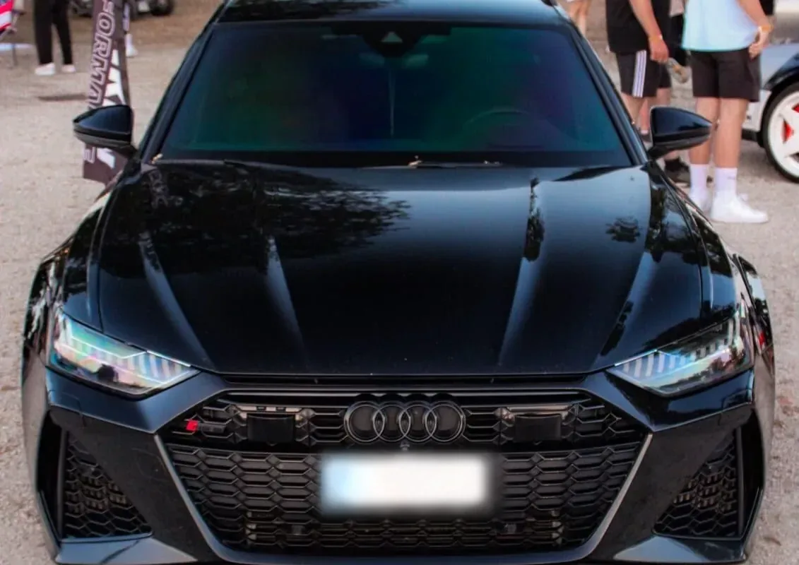 Schwarzer Audi RS6 C8 Avant frontal auf einem Tuning-Treffen, im Hintergrund Besucher und weitere Fahrzeuge