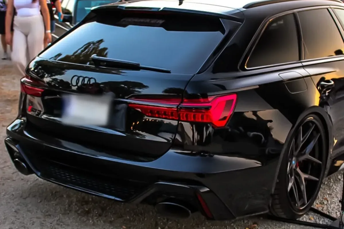 Heck des schwarzen Audi RS6 C8 Avant auf einem Tuning-Treffen vor einer Halle, daneben eine Fahne von Franken Performance