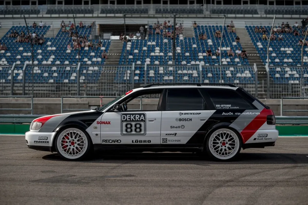 Audi S6 C4 Avant in Audi-DTM-Design-Folierung mit Startnummer 88 vor der Tribüne einer Rennstrecke, Seitenansicht