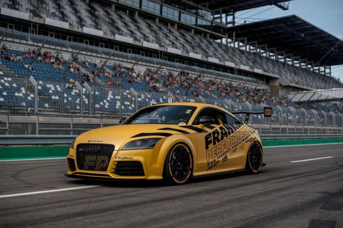 Gelber Audi TT RS 8J mit Franken-Performance-Beklebung und Heckflügel auf einer Rennstrecke vor der Tribüne