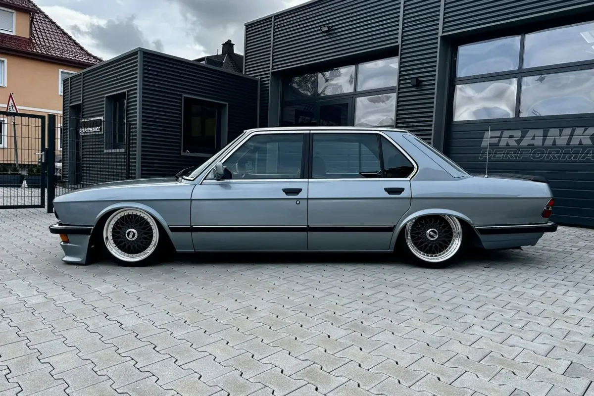BMW E28 518i in Seitenansicht von links, tiefergelegt auf BBS-Felgen vor dem dunklen Werkstattgebäude mit Franken-Performance-Schriftzug