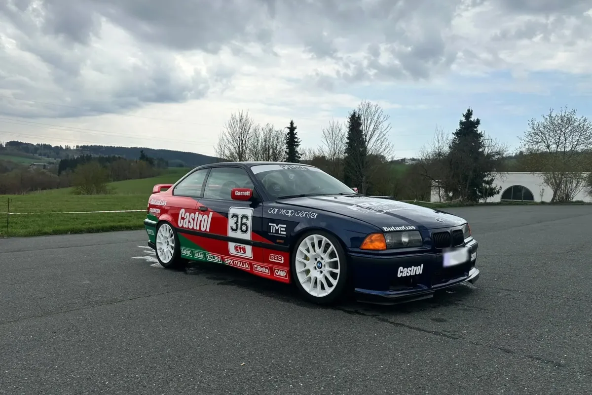 BMW E36 Coupé im Castrol-Design mit Startnummer 36 und Frontspoilerlippe, schräg von vorne auf einem Parkplatz unter bewölktem Himmel