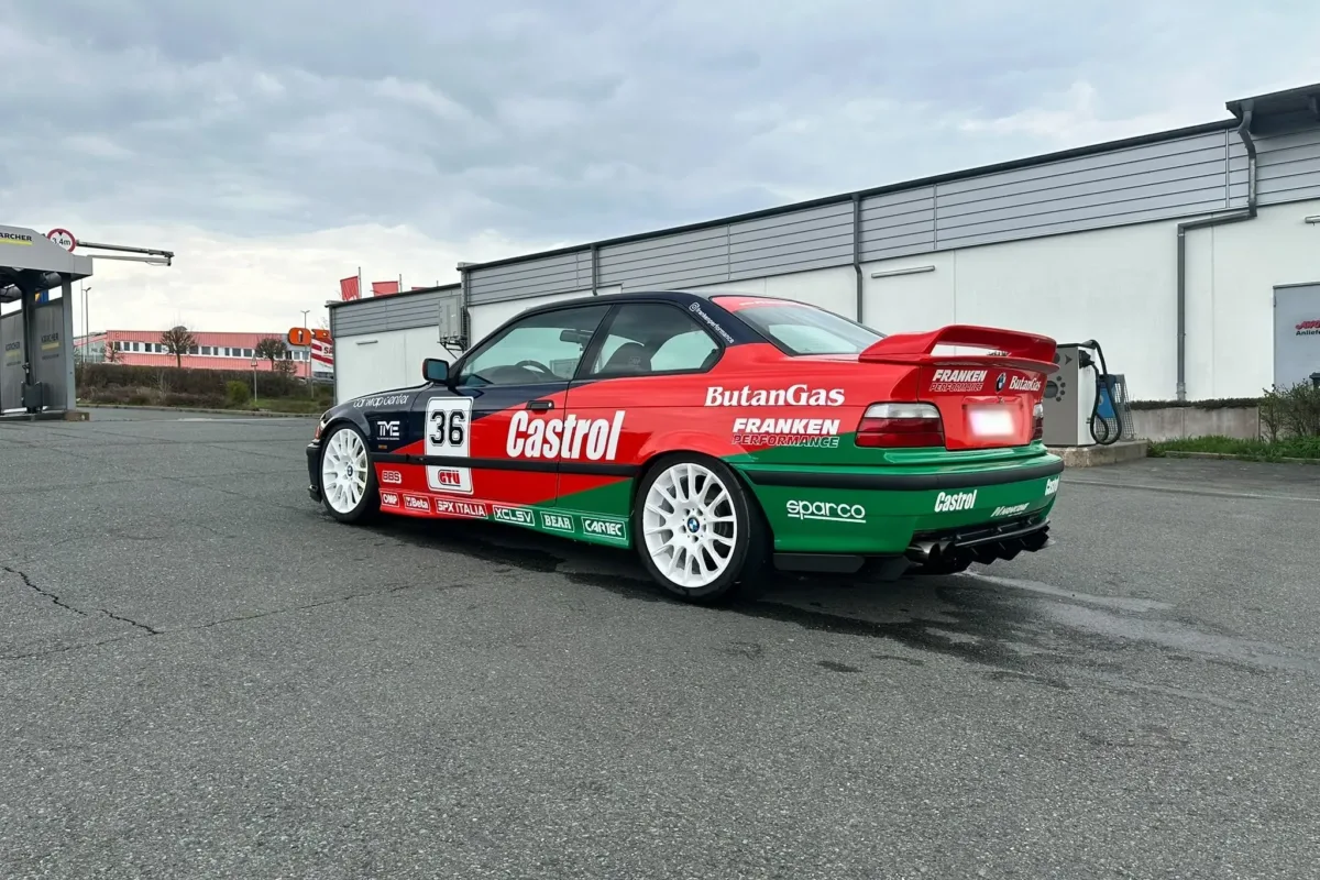 BMW E36 Coupé im Castrol-Design schräg von hinten mit rotem Heckflügel, Franken-Performance-Schriftzug und Heckdiffusor
