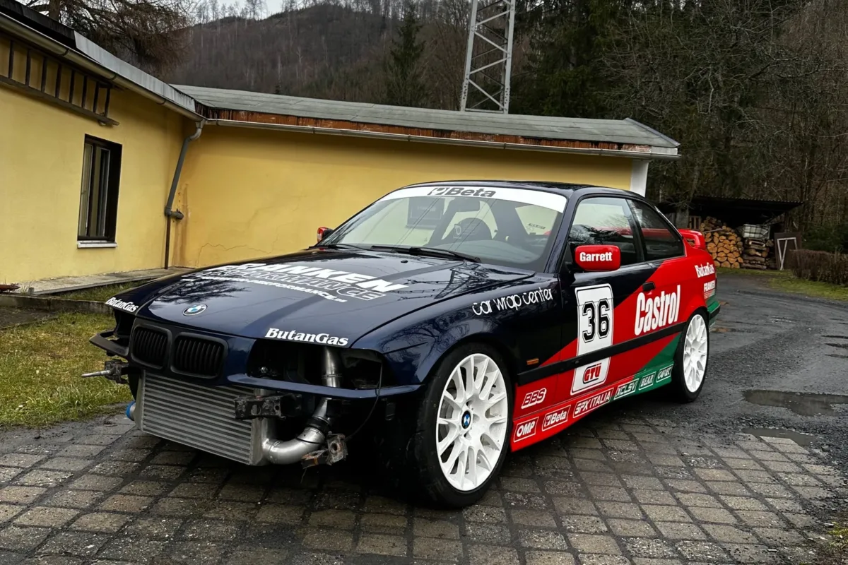 BMW E36 Coupé mit Startnummer 36 und Ladeluftkühler vor einem gelben Gebäude, schräg von vorne