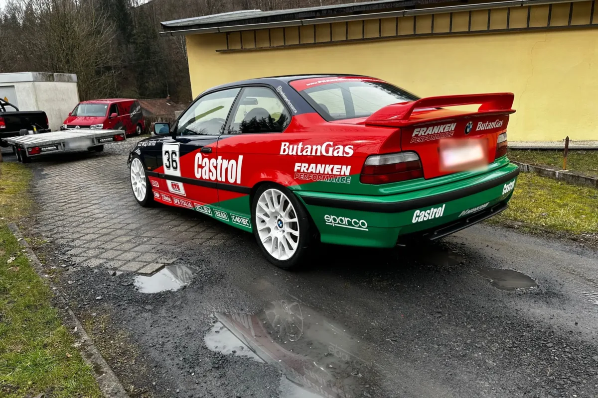 BMW E36 Coupé in Motorsport-Folierung mit Startnummer 36 und weißen Felgen, schräg von hinten