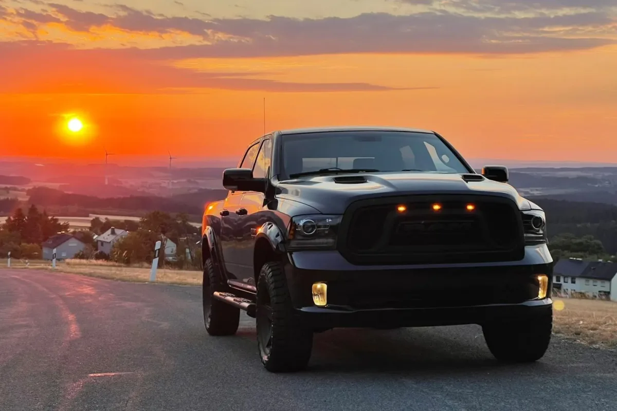 Dodge RAM 1500 frontal im Gegenlicht der tief stehenden Sonne, im Kühlergrill leuchten drei orangefarbene Positionsleuchten
