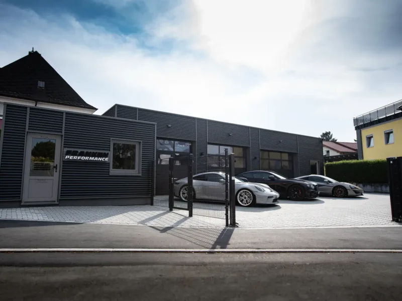 Firmengebäude von Franken Performance mit dunkler Metallfassade, davor drei Sportwagen auf dem gepflasterten Hof