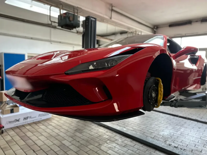 Roter Ferrari F8 Spider auf der Hebebühne in der Werkstatt, Vorderrad abgenommen, Bremsscheibe und gelber Bremssattel sichtbar