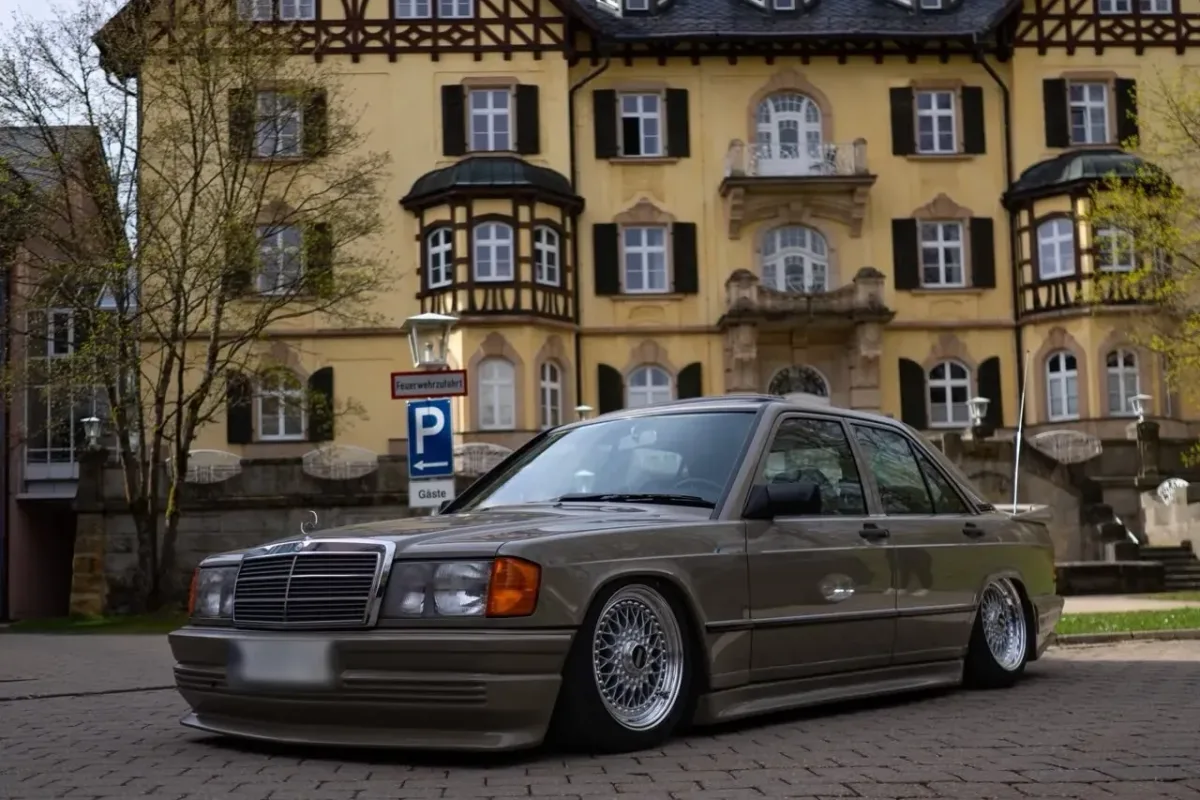 Tiefergelegter Mercedes-Benz 190 (W201) mit Zender-Bodykit und BBS-RS-Felgen vor einem gelben historischen Gebäude mit Fachwerk-Obergeschoss und Dachgauben