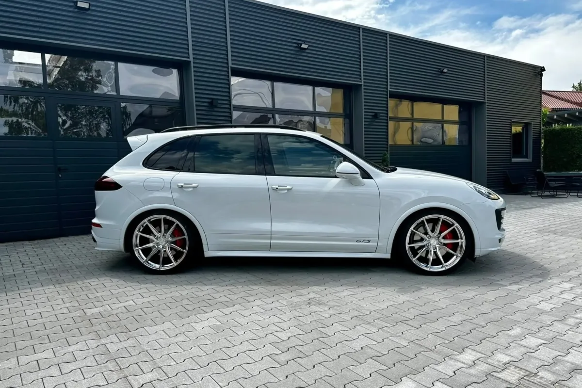 Seitenansicht des weißen Porsche Cayenne GTS mit GTS-Schriftzug, tiefergelegt auf silbernen Vossen-Felgen vor dem Werkstattgebäude