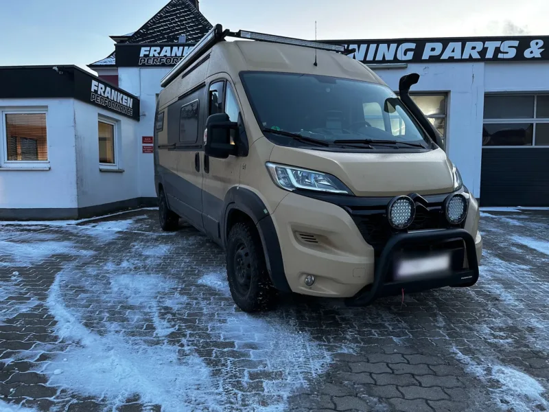 Sandfarbener Citroën-Jumper-Kastenwagen mit Frontbügel, LED-Zusatzscheinwerfern und Geländereifen im Schnee vor der Werkstatt von Franken Performance