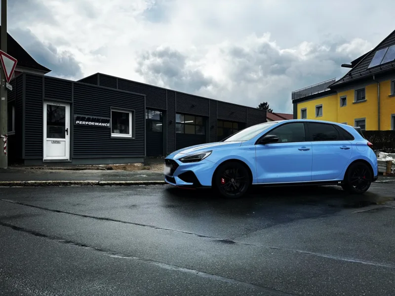 Hellblauer Hyundai i30 N mit schwarzen Felgen und roten Bremssätteln vor dem dunklen Werkstattgebäude von Franken Performance