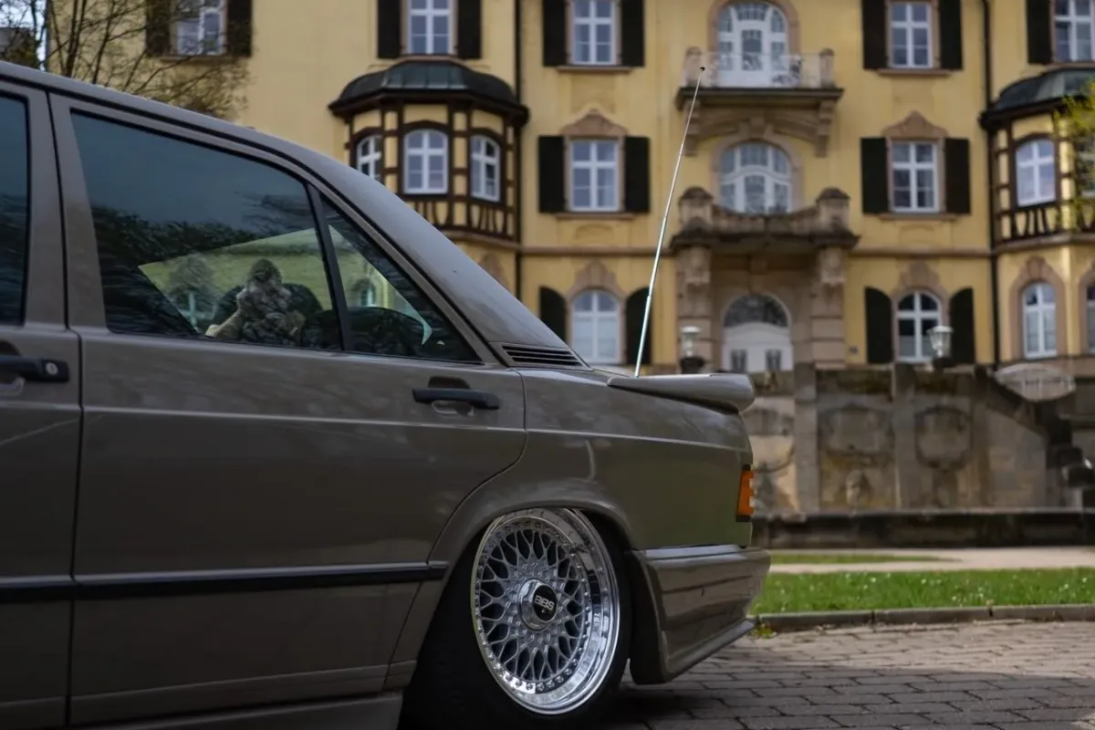 Mercedes-Benz 190 (W201) mit Zender-Bodykit und BBS-RS-Felge, Seitenpartie aus niedriger Perspektive vor einem historischen Gebäude mit Fachwerk-Obergeschoss