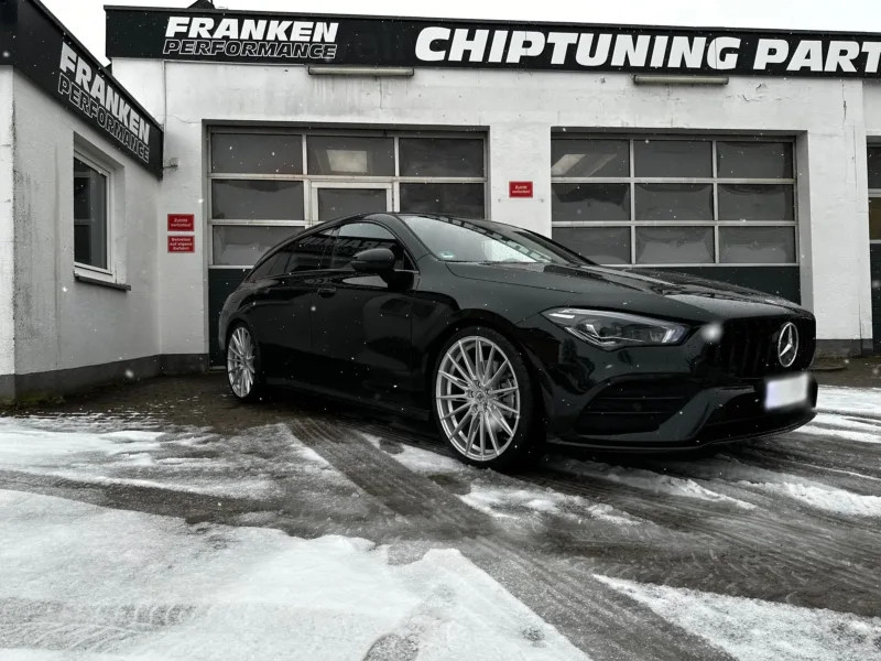 Schwarzer Mercedes-Benz CLA mit AMG-Kühlergrill und silbernen Vielspeichenfelgen im Schnee vor der Werkstatt von Franken Performance