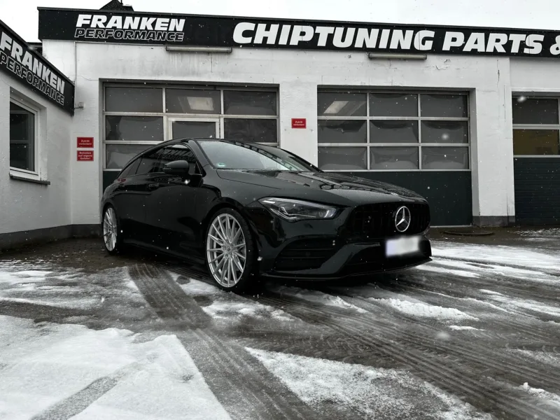 Schwarzer Mercedes-Benz CLA mit AMG-Kühlergrill im Schnee, Frontansicht vor der Werkstatt von Franken Performance