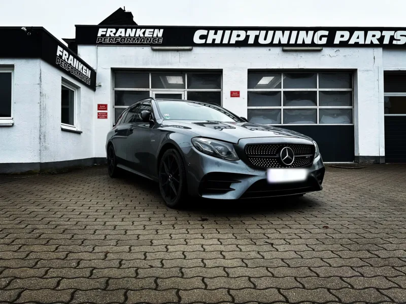 Grauer Mercedes-Benz E-Klasse T-Modell mit AMG-Frontschürze und schwarzen Felgen vor der Werkstatt von Franken Performance