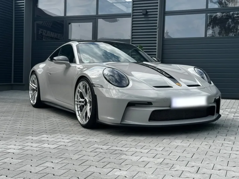 Grauer Porsche 911 (992) GT3 Touring mit schwarzem Porsche-Schriftzug auf der Fronthaube vor dem dunklen Werkstattgebäude von Franken Performance