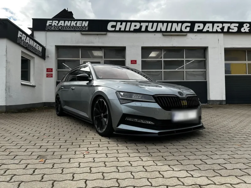 Grauer Škoda Superb Combi mit schwarzen Felgen und Frontspoilerlippe vor der Werkstatt von Franken Performance