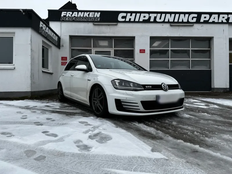 Weißer VW Golf 7 GTD im Schnee, schräg von vorne vor der Werkstatt von Franken Performance